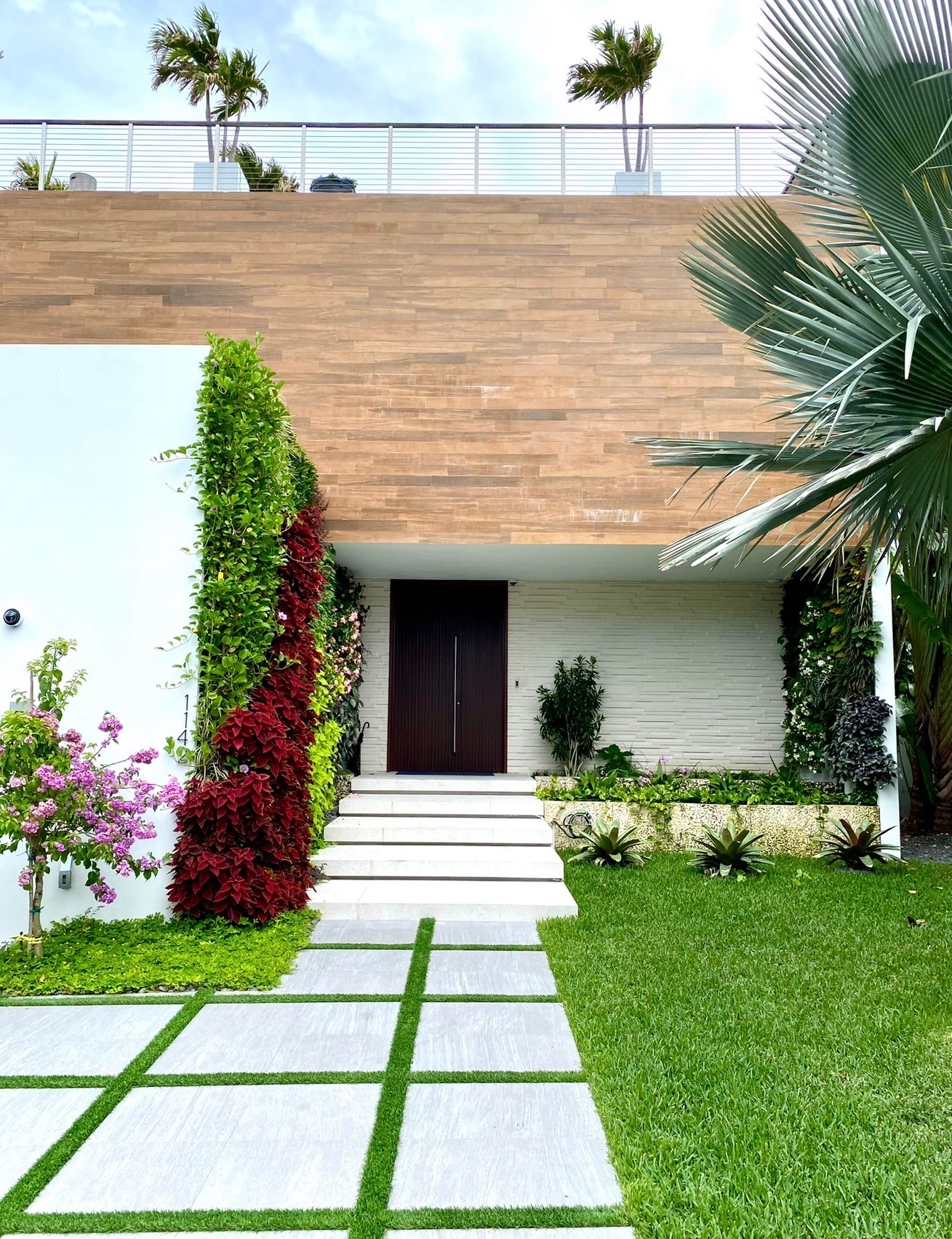 Same entrance transformed with a lush vertical living wall of greenery and red coleus, flowering bougainvillea, and grass-joint pavers