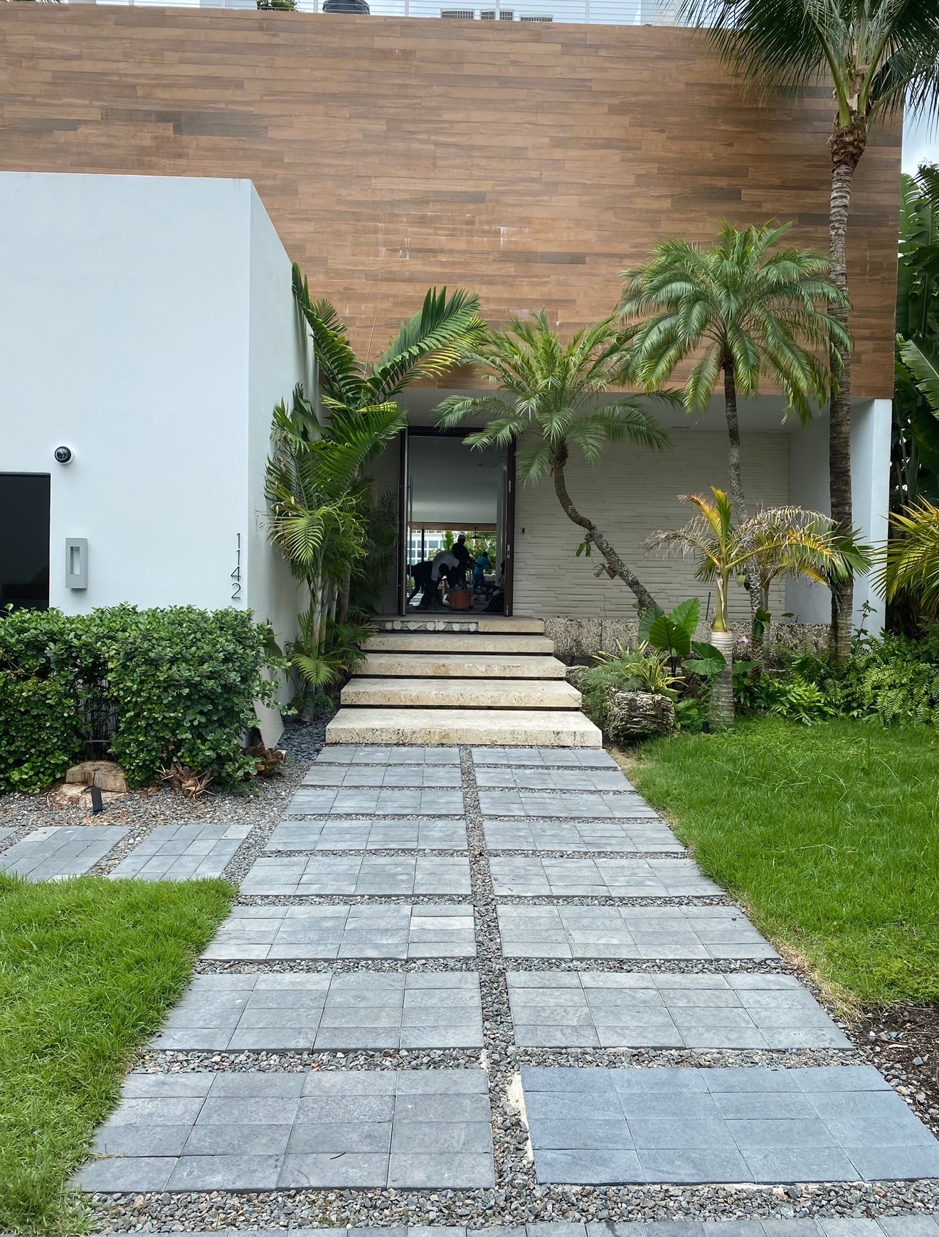 Modern home entrance with a plain white facade, gravel-joint gray pavers, and clipped hedges before planting